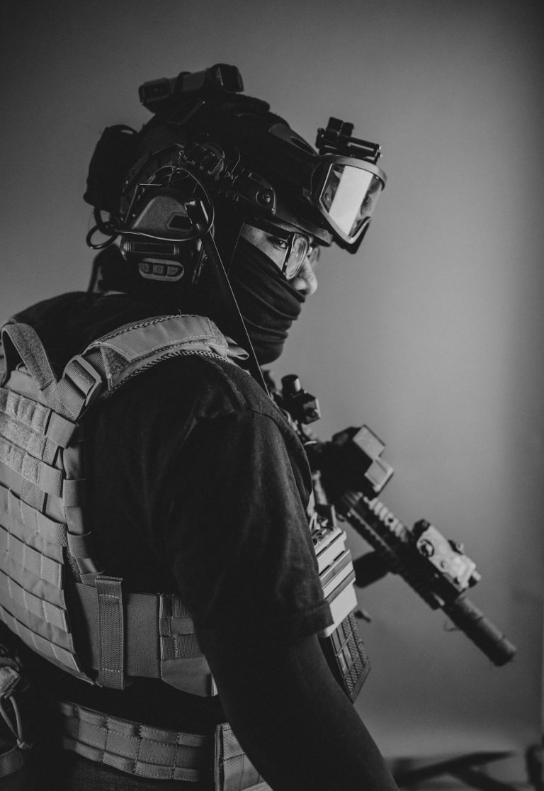 Black and white portrait of a soldier in tactical gear holding a rifle ready for action.