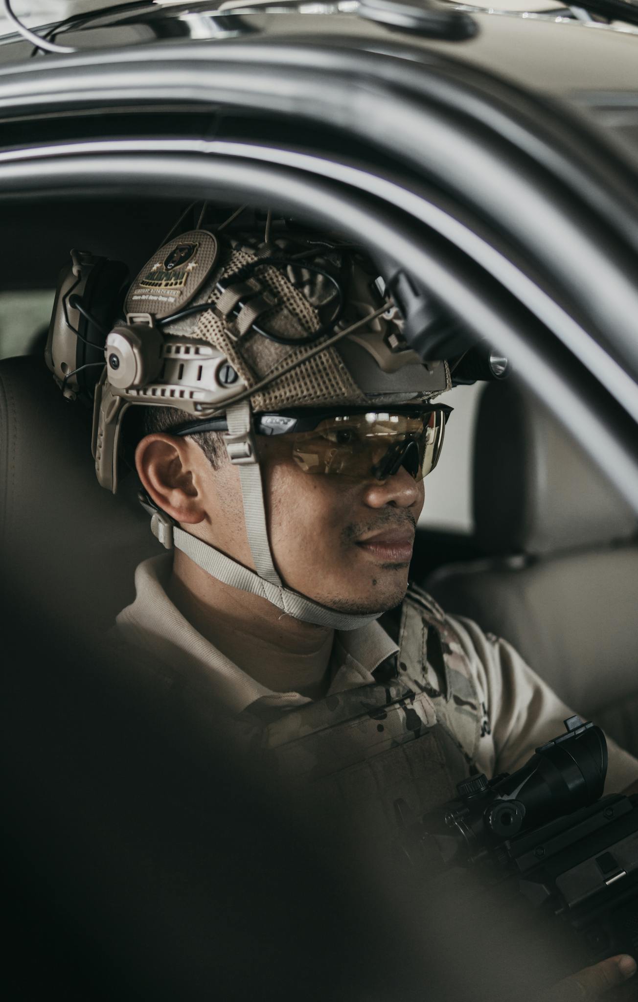 Close-up of a soldier in tactical gear wearing a helmet and protective eyewear inside a vehicle.